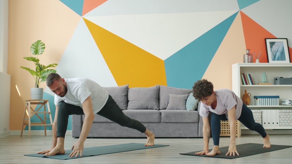 Woman and man are working out at home doing yoga together synchronously on mats caring for body health. Modern people, sports and apartment concept.